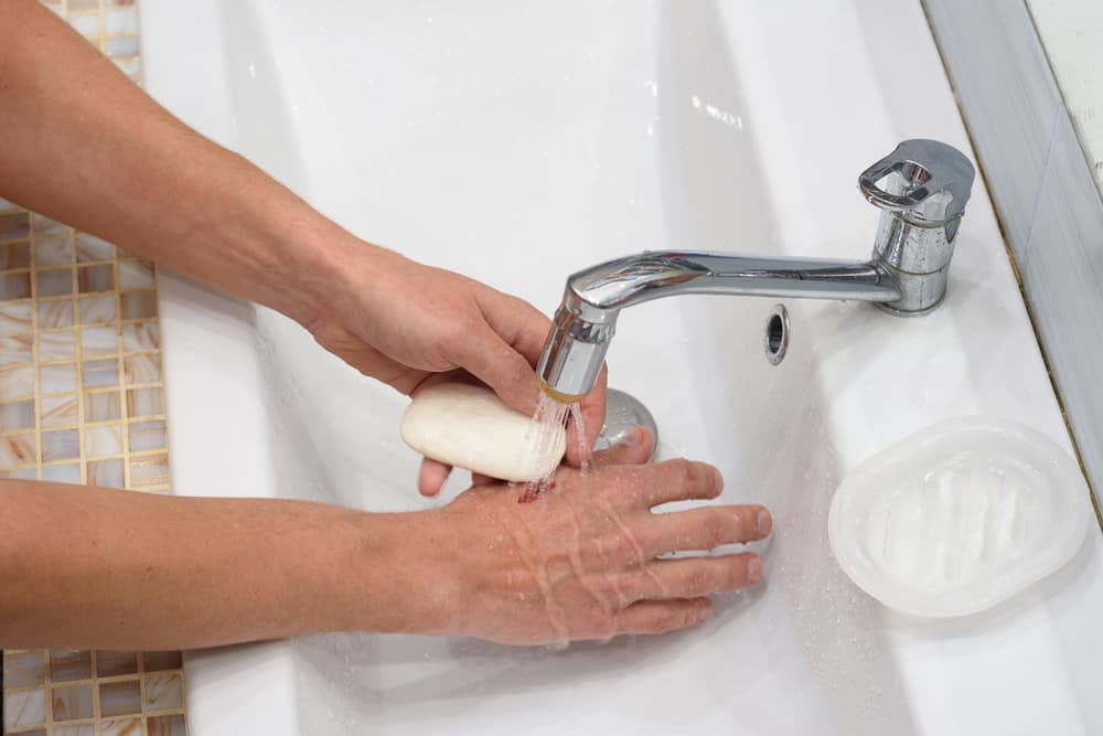A man provides first aid for cutting his hands, washing the wound with soap