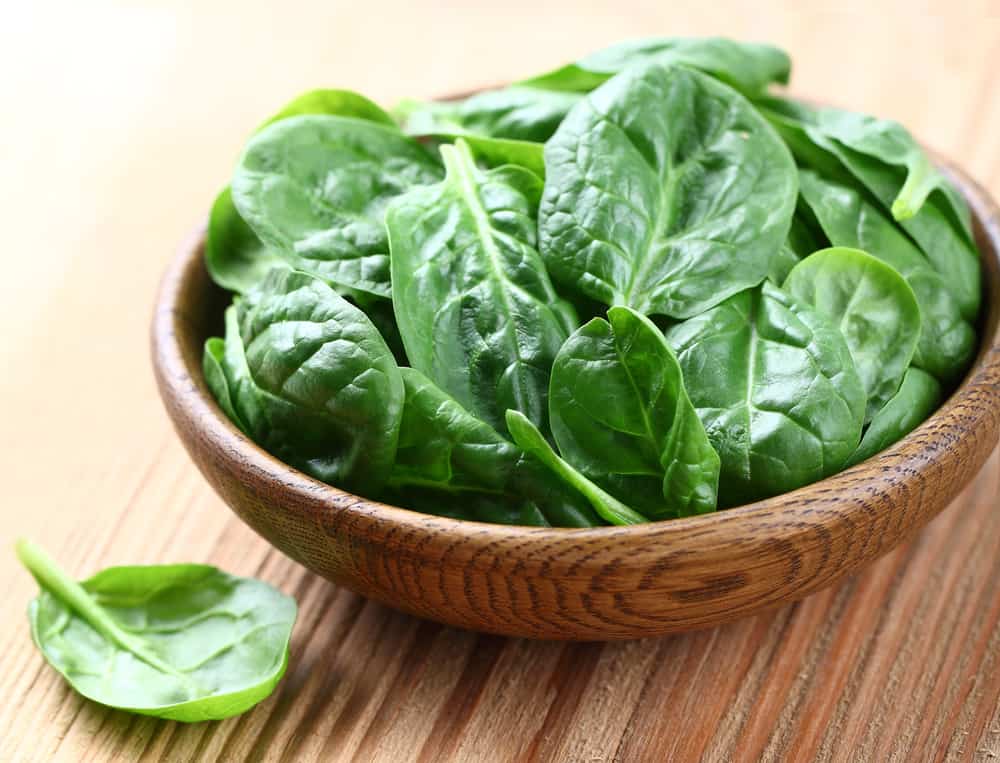wooden bowl containing baby spinach leaves