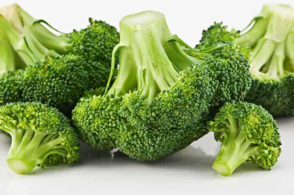 several raw broccoli with stems against a white background